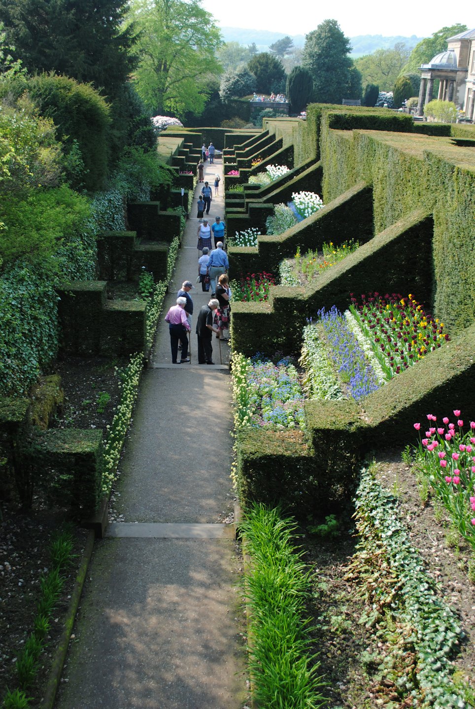 Persone passeggiano lungo un sentiero di ghiaia in un giardino formale.
